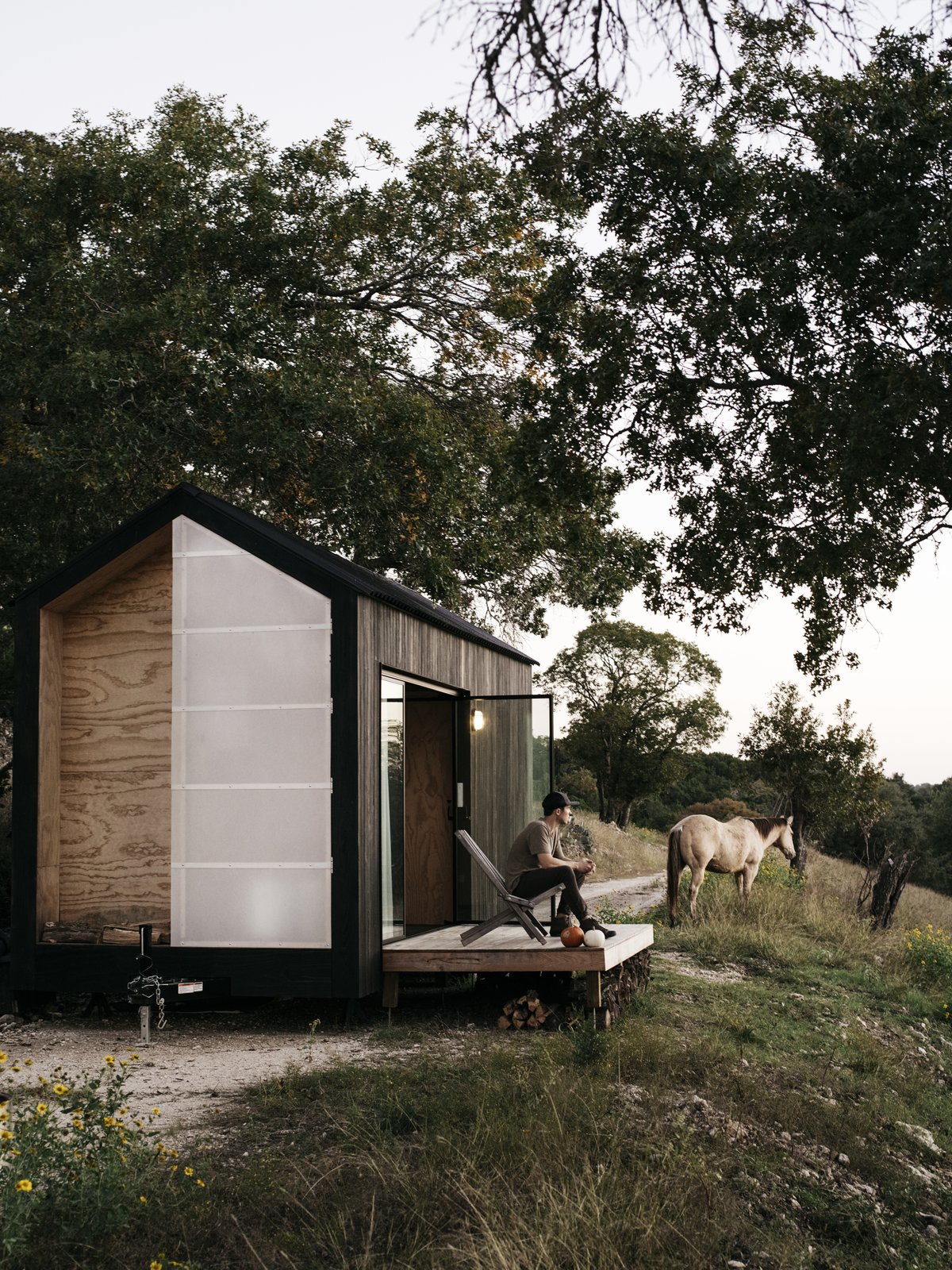 Ryan McLaughlin watches the sunset from the deck of the 160-square-foot tiny home he built, with no prior experience, at his parents’ horse ranch in Georgetown, Texas. Soon, the trailer-mounted cabin will be moved to a vineyard, where it will operate grid-free and be available to rent for short stays.